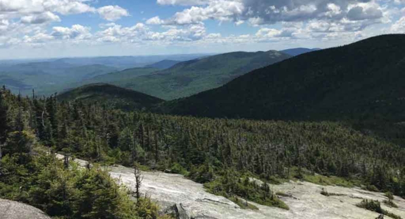 the Appalachian mountains of maine appear vast and green below a blue sky dotted with clouds